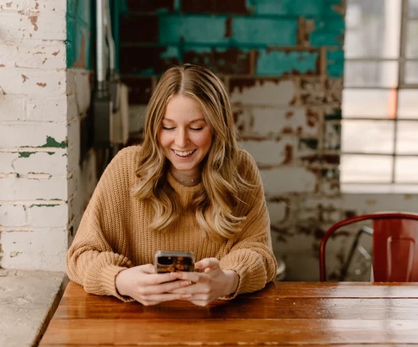 Femme souriante qui consulte une plateforme de rencontre sur son téléphone dans un café
